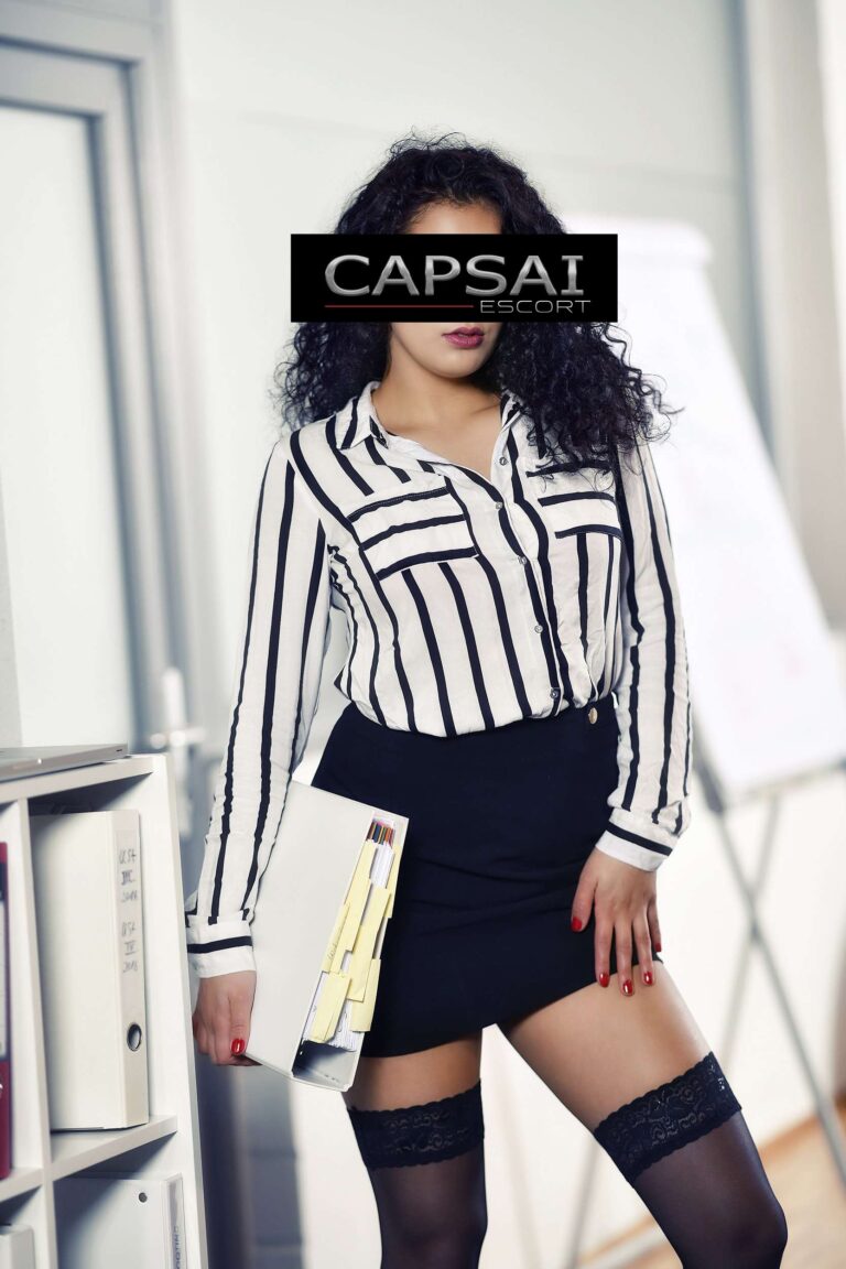 Escort Dame Alessia in einer schwarze/weißen Blus mit einem schwarzen Rock und schwarzen Nylons.