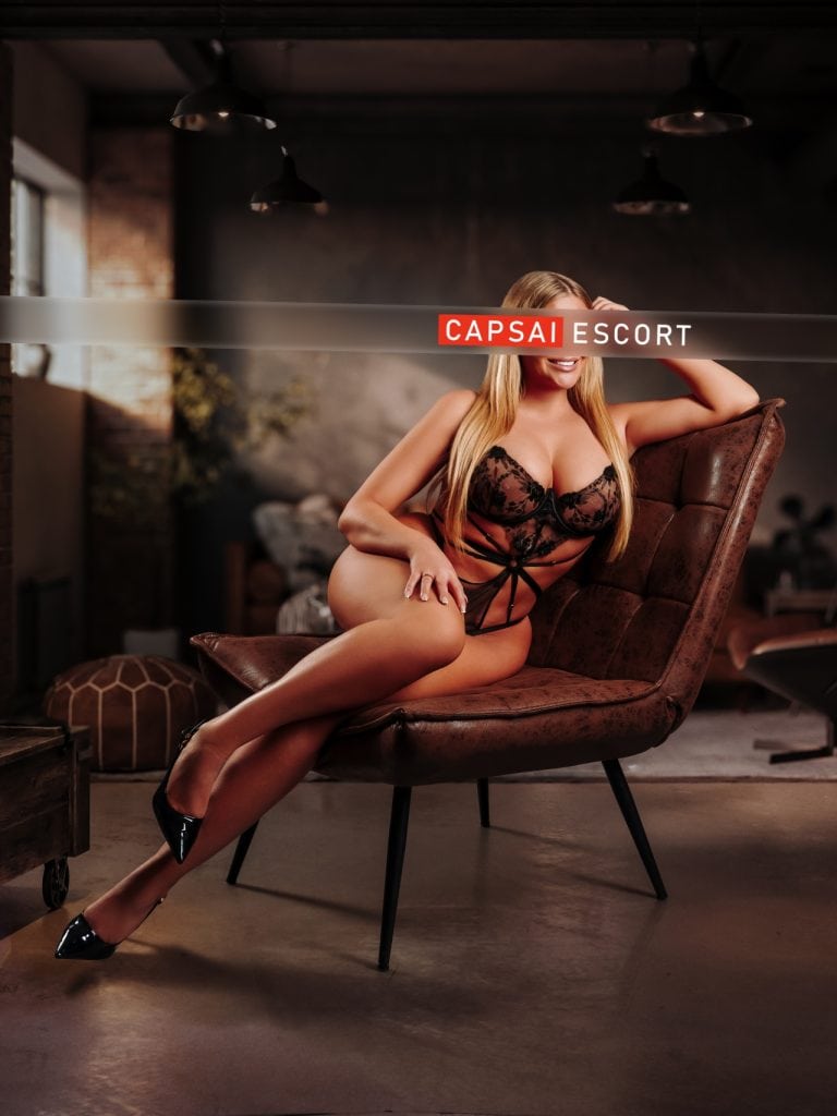 Escort Alina in schwarzem Spitzenbody auf einem braunen Ledersessel