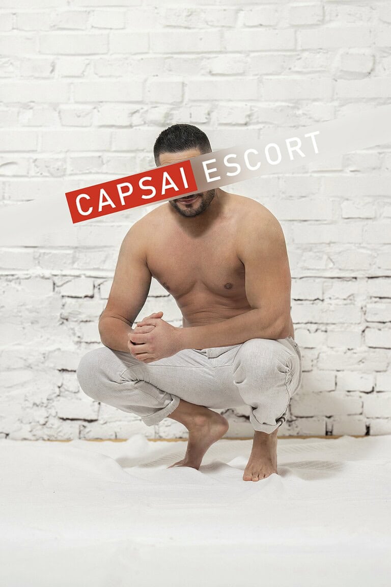 Callboy Carlos oberkörperfrei und Hose in hockender Pose.