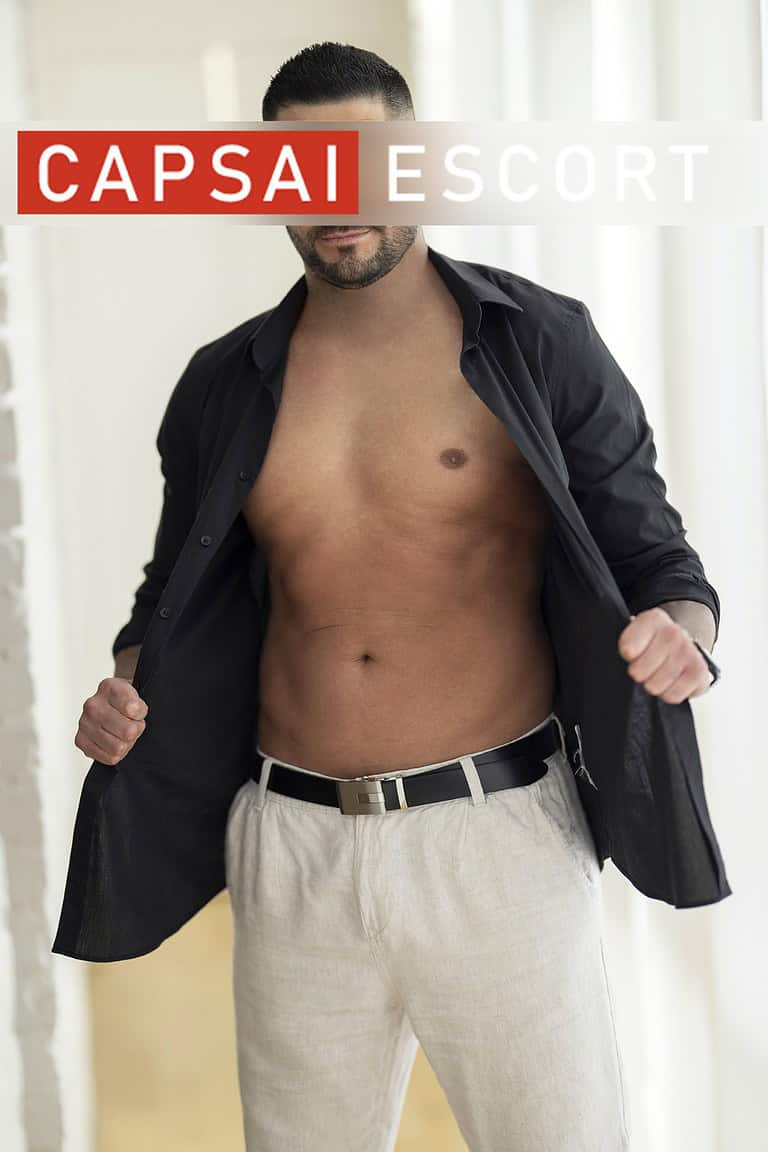 Callboy Carlos mit offenem Hemd und Hose in stehender Pose.