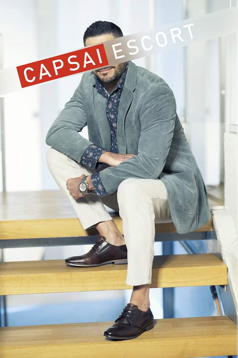 Callboy Carlos im Sakko und Cordhose auf der Treppe sitzend.