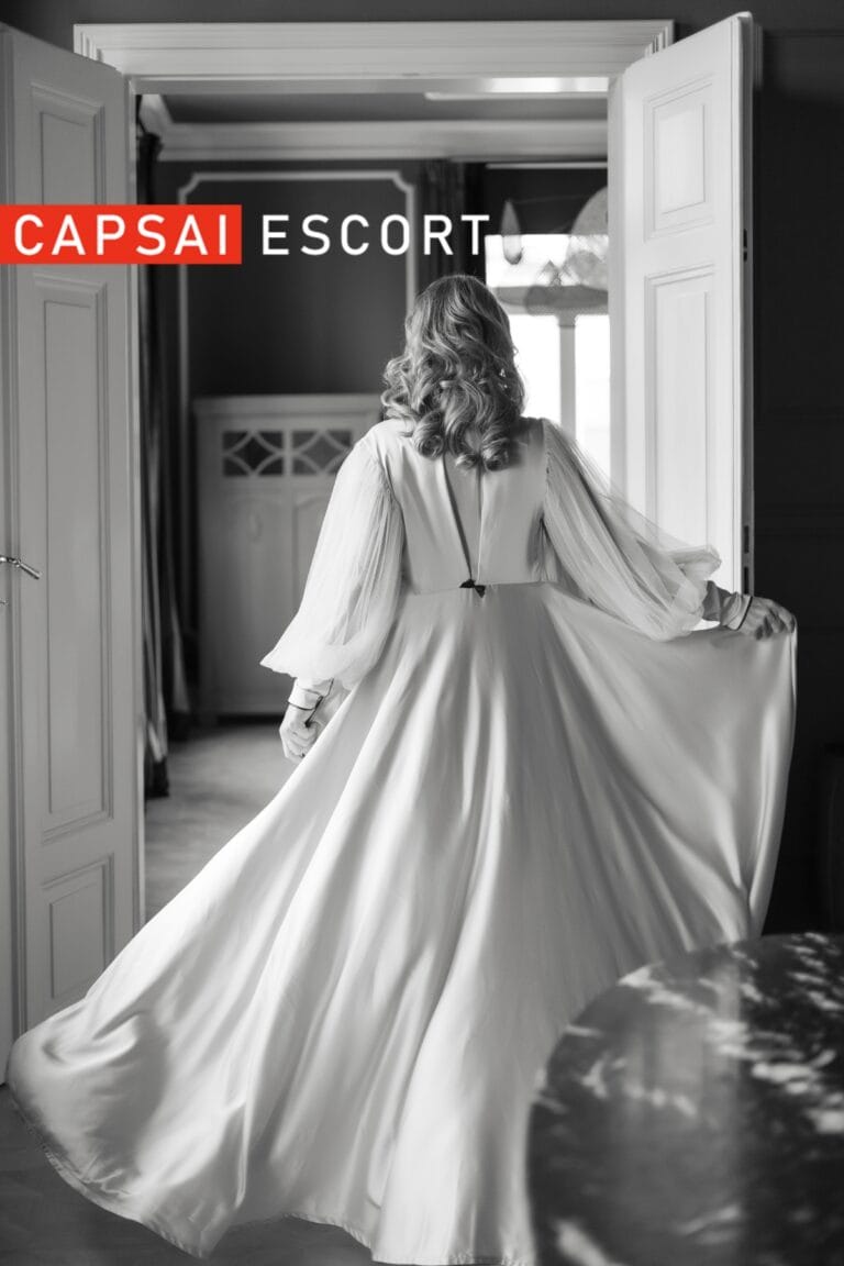 Escort Dame Freya in einem langen weißen Morgenmantel, mit Ansicht von hinten.