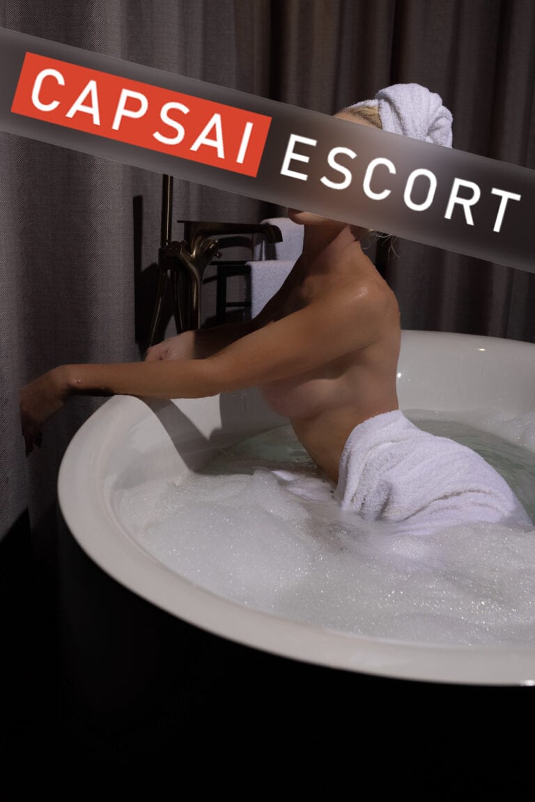 Escort Dame Aurelia oben ohne und einem Handtuch um die Hüfte gewickelt in der Badewanne.
