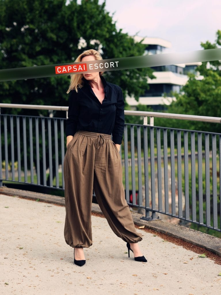 Escort Marlene in schwarzer Bluse und weiter Hose am Geländer