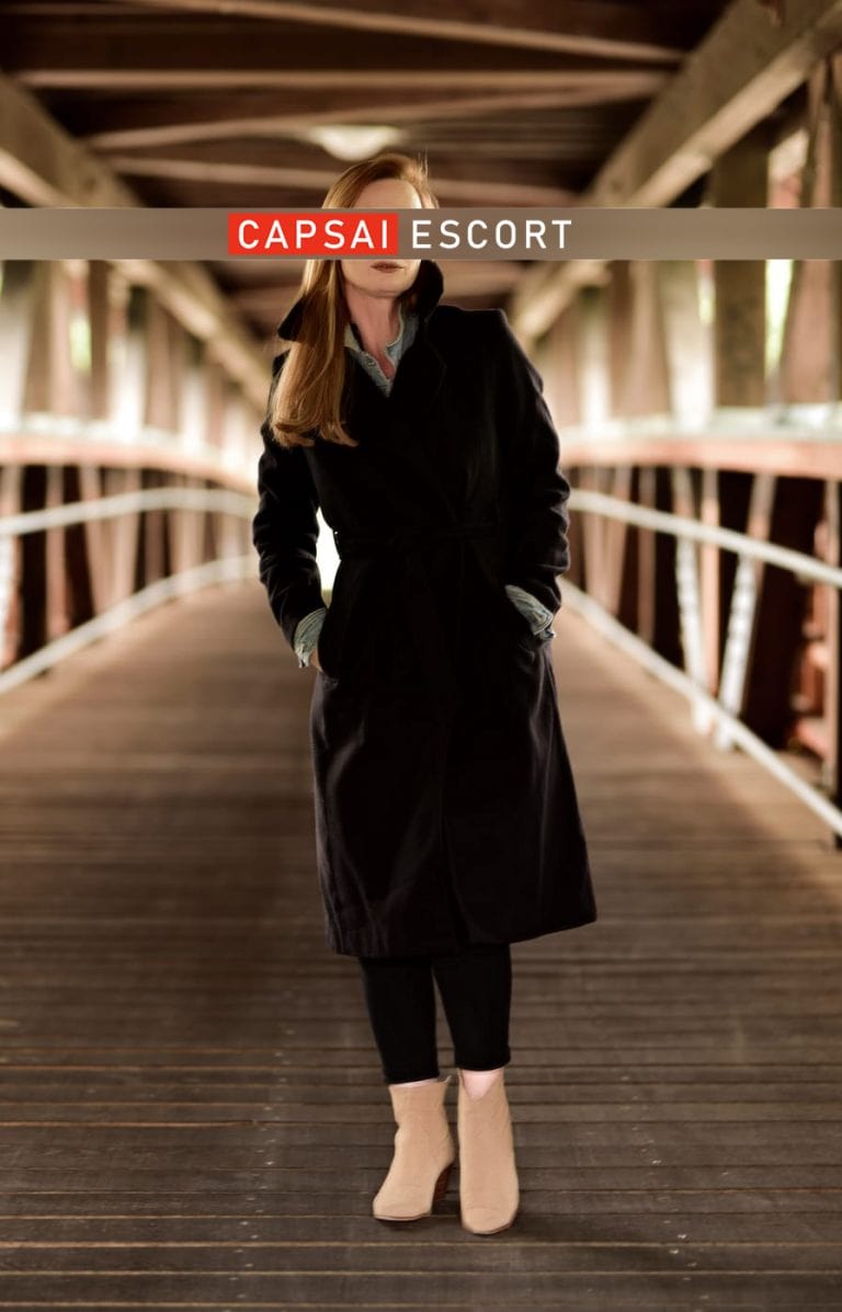 Escort Dame Marlene im schwarzen Mantel und schwarzer Hose auf einer Brücke stehend.