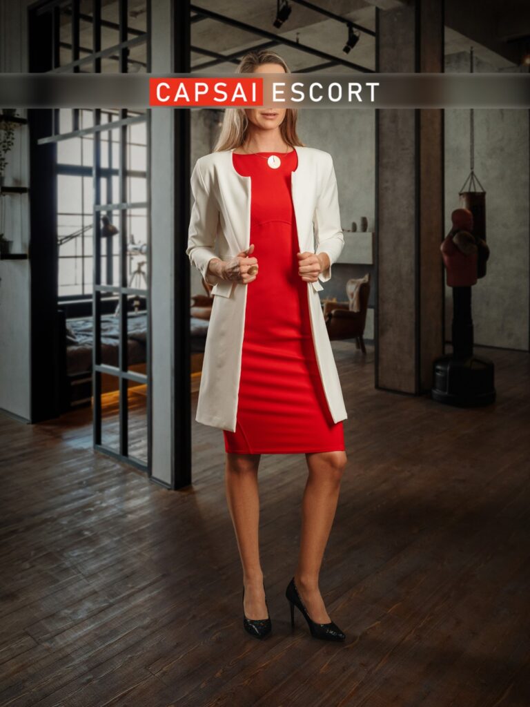 Escort Dame Svea in einem roten Kleid und schwarzen High Heels und weißem Mantel.