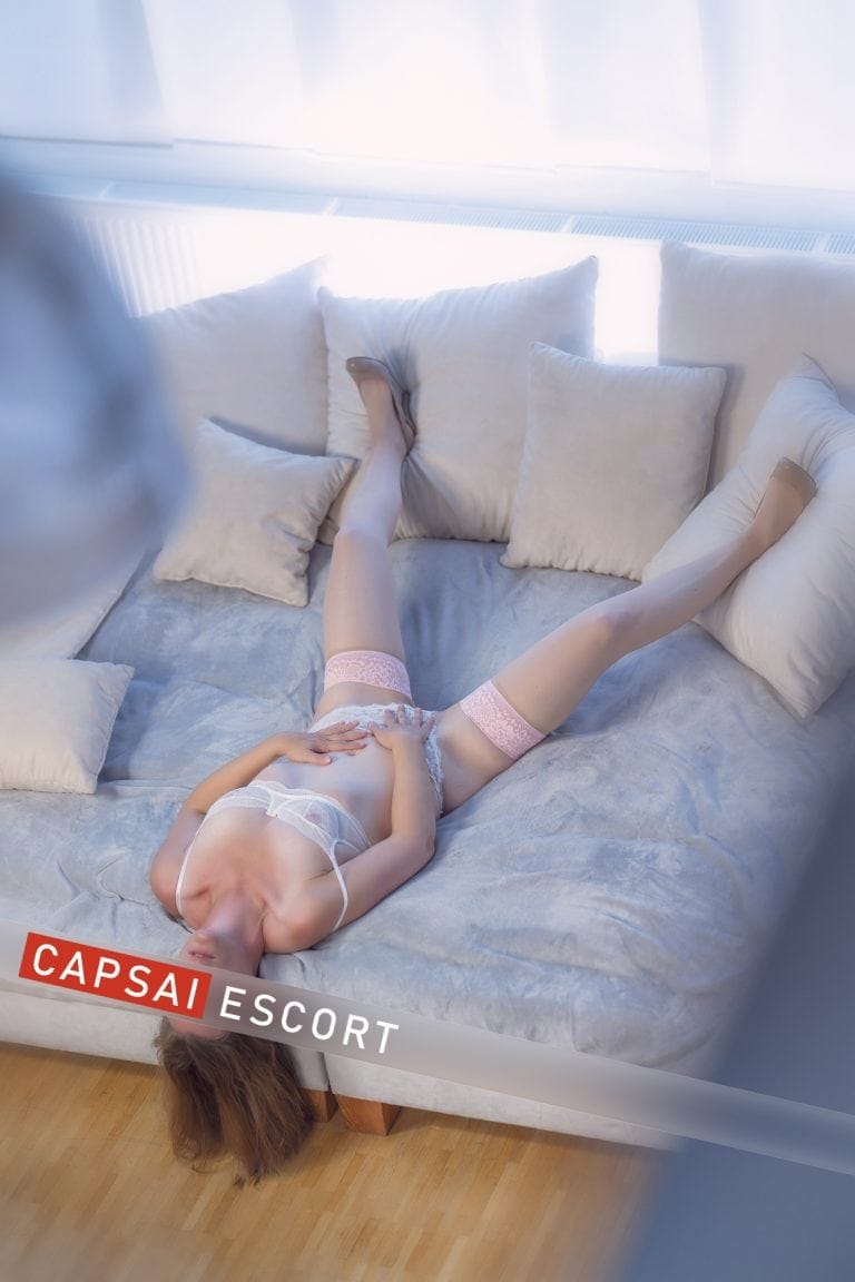Escort Dame Thea weißen transparenten Dessous und Nylons mit High Heels breitbeinig auf dem Sofa liegend.