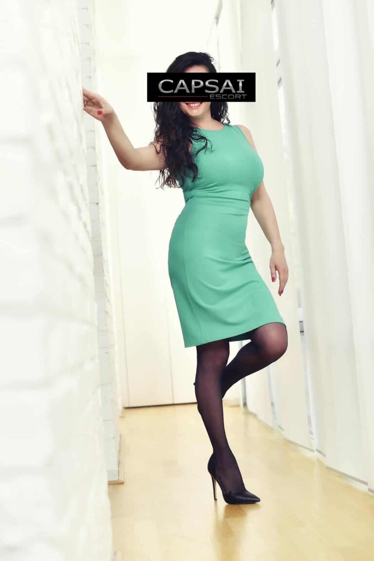 Escort Dame Kate in einem grünen Kleid mit schwarzen Nylons und schwarzen High Heels.